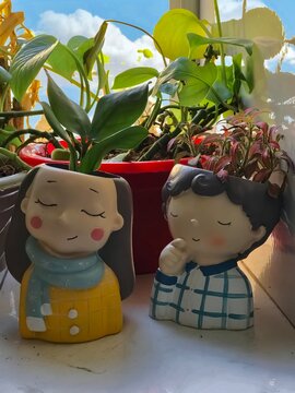 Cute couple-shaped planters with lush green plants sit on a sunny windowsill, against a bright blue sky. A charming touch of nature. 100% processed with my only devide iPhone 7 plus 32G .