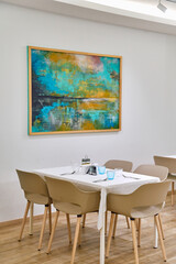 Modern Dining Space Featuring a Vibrant Abstract Painting on the Wall Alongside Minimalist Furniture and Elegant Table Settings