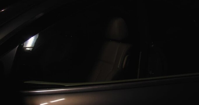 A car thief in black gloves pulls the car door handle at night, trying to rob or steal a car, and gets in.Concept for advertising the installation of alarm systems or guarded parking