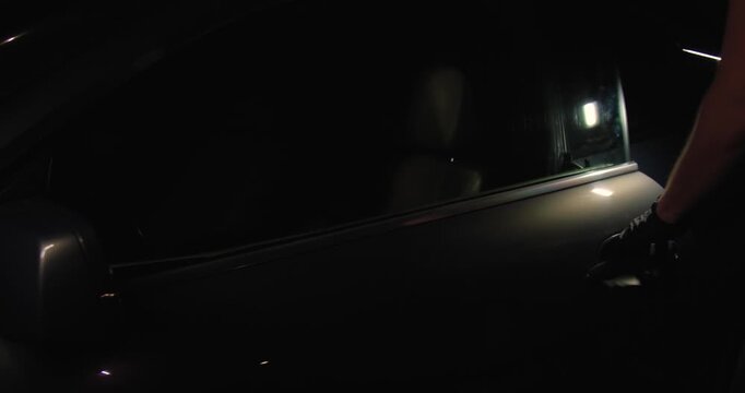 A car thief in black gloves pulls the car door handle at night, trying to rob or steal a car, and gets in.Concept for advertising the installation of alarm systems or guarded parking