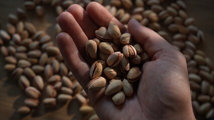 Hand holding pistachios above scattered pile on table