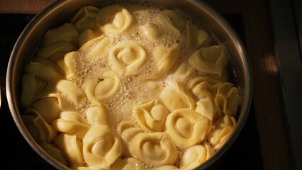 Top view of boiling tortelloni in saucepan beside tomato sauce