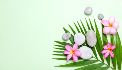 Tropical spa arrangement with smooth gray stones and pink plumeria flowers on green palm leaf, creating calm and refreshing atmosphere for relaxation and wellness