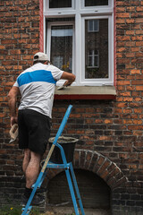 A man on a ladder puttying a window sill