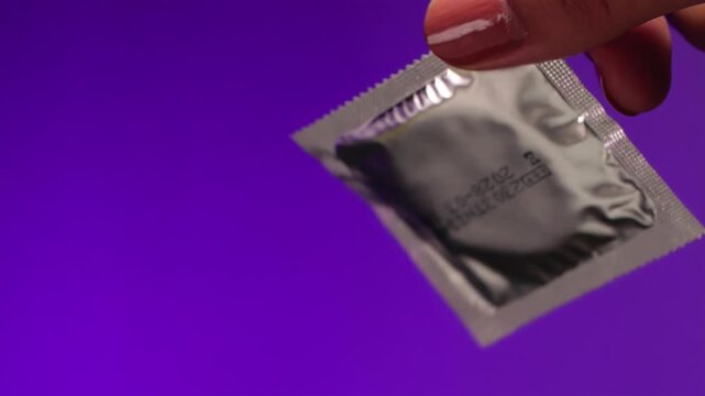 Extreme close-up female hamd  holding  sealed condom   on a lilac background