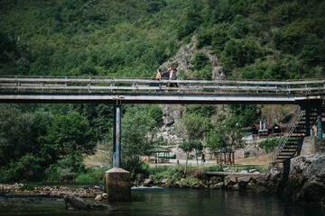 A group of people walking peacefully across a bridge surrounded by lush greenery and water under a bright sunny day.