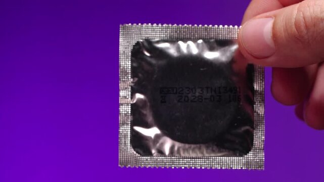 Extreme close-up male hamd  holding  sealed condom   on a lilac background