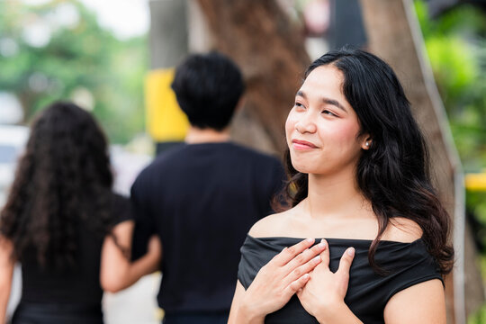 Content woman places hand on chest and smiles warmly while watching her ex-boyfriend walk away with his new girlfriend on the street.