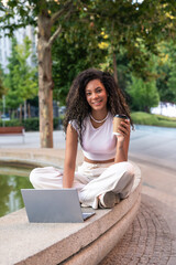 Naklejka premium Young woman working remotely in urban park enjoying coffee break