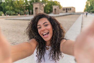 Tourist taking a selfie with both hands in front of the Temple of Debod in Madrid, enjoying a warm summer day