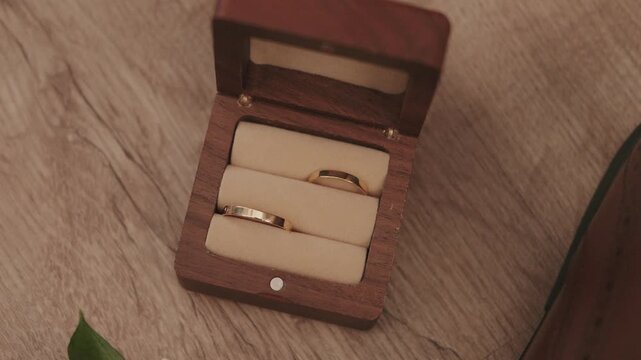 Close up of two gold wedding rings in a wooden ring box on a wooden surface during wedding prep
