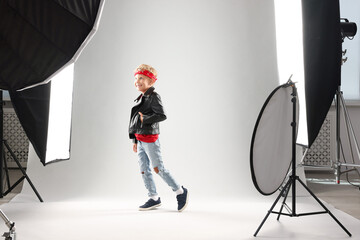 Little boy on light grey background in photo studio with professional equipment