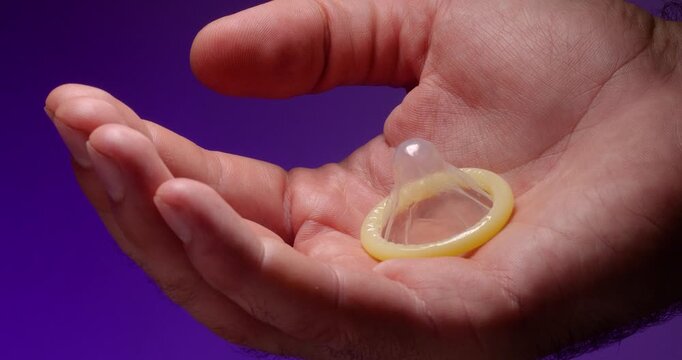 Super close-up of a male palm holding an unused condom on a lilac background