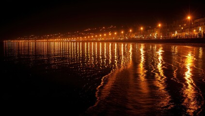 Obraz premium Lit coastal promenade at night, streetlights reflect off water, horizon buildings