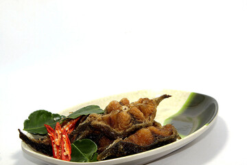 Traditional fried catfish garnished with kaffir lime leaves and red chili on a plate. On a white backdrop