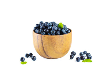 Ripe fresh blueberries with leaves in wooden bowl isolated on white.