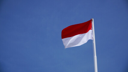 The red and white flag fluttering high fluttered in the wind in the air against the backdrop of a cloudy blue sky