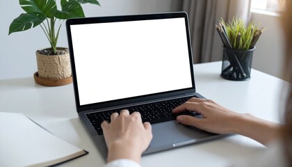 A person working on a laptop, keyboard view close up. The screen is illuminated brightly, set on a desk with other stationary