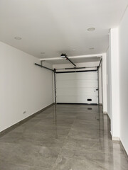 Modern garage with a white automatic door and polished gray tiled flooring.