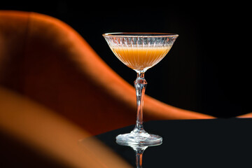 Stylish cocktail in crystal glass on black reflective table in moody bar