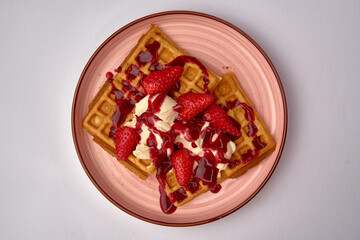 Deliciously Indulgent Waffles Topped with Fresh Strawberries and Cream, Drizzled with Rich Berry Sauce on a Stylish Plate