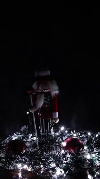 Una toma de cerca de un soldadito de juguete o cascanueces de navidad rodeado de bolas de navidad y luces de color blancas. Decoraci&oacute;n de navidad y fin de a&ntilde;o. Video vertical