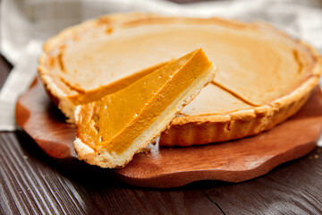 Pumpkin pie with a slice removed, showcasing creamy filling and golden crust, placed on a wooden board, evoking warmth and comfort of homemade desserts
