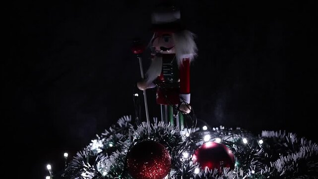 Una toma de cerca de un soldadito de juguete o cascanueces rodeado de bolas de navidad y luces de color blancas. Decoraci&oacute;n de navidad y fin de a&ntilde;o