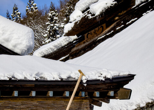 雪おろし棒を使って屋根から雪を下ろしている作業風景