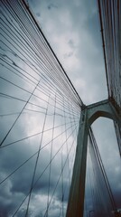 Obraz premium Suspension bridge tower and cables against a cloudy sky, looking up in vertical format