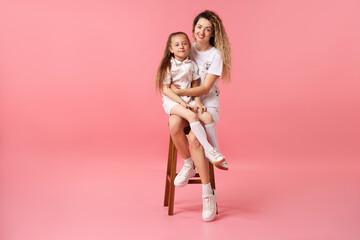 Family. Happy mother and her daughter posing on stool against pink background
