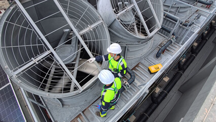 Workers maintain large cooling fans on industrial roof during bright day in city © FotoArtist