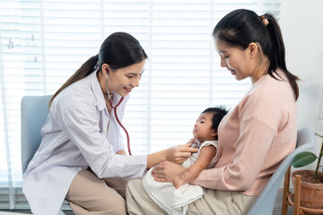 Obraz premium Smiling female pediatrician listens to newborn’s heartbeat with stethoscope, fostering trust and comfort while providing expert care during a warm mother-baby clinic visit.