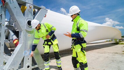 Workers inspect wind turbine components under a clear sky at a renewable energy site