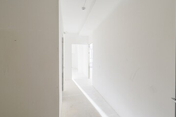 bright, empty hallway with white walls leads into the distance. Light streams in, illuminating the bare floor