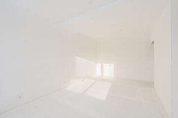 empty, all-white room with light streaming through a window. The walls are smooth, and there are electrical outlets on them