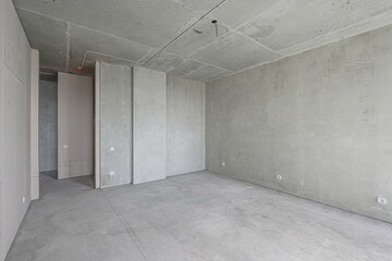 empty, unfinished room with bare concrete walls, floor, and ceiling. Electrical wiring is visible