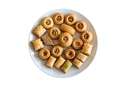 Middle Eastern mamoul cookies and assorted baklawa. Seen from above. Arabic baked treats with nuts on a white plate on a dark wooden table. Cookies for the Ayd El Fithr celebration.

