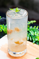 Iced preserved lime soda in a clear glass with crushed ice and mint leaves, served on a wooden surface with a green leafy background.