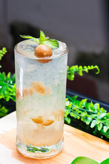 A refreshing glass of iced preserved plum soda garnished with mint leaves, served on a wooden surface with a green background.