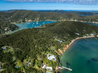 Aerial view of boats sailing in the bay, surrounded by lush green hills and luxury homes in Kawau...
