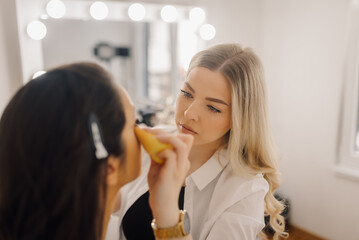 Makeup artist applying foundation on model's face in beauty salon