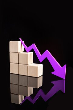 A purple downward zigzag arrow next to with stacked wooden blocks, symbolizing a declining trend on a reflective black surface. High quality photo