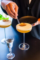 Bartender garnishing passion fruit cocktails with tweezers in elegant coupe glasses on bar counter,...