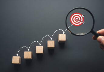 Photo of magnifying glass focusing on target with arrows representing steps to achieve business goals