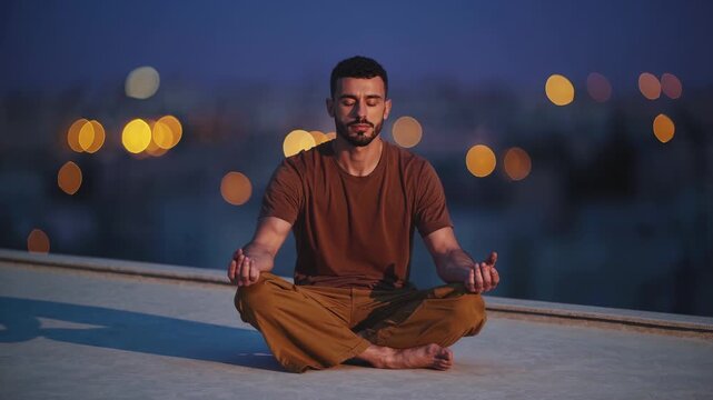 Man doing yoga meditation outdoors. Peaceful rooftop night practice. Man sits in focus pose. Calm meditation with focus. Yoga on rooftop brings peaceful night and mindfulness to man evening routine.