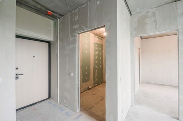 room under construction shows bare walls, door frames without doors, and a front door. The space has a raw, unfinished look