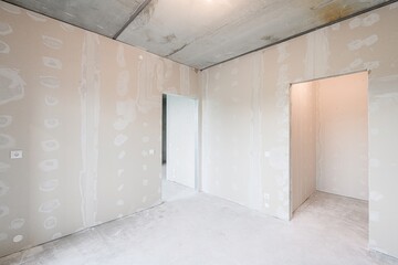 room under renovation with bare walls, concrete ceiling and floor. Doorways lead to other unfinished spaces