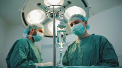Medical surgeons in sterile surgical room wearing green scrubs and masks performing procedure under bright operating lights with IV fluid drip, representing modern healthcare, teamwork, and surgery