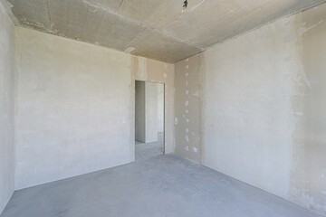 An empty, unfinished room with concrete walls, floor, and ceiling, and a doorway leading to another similar room